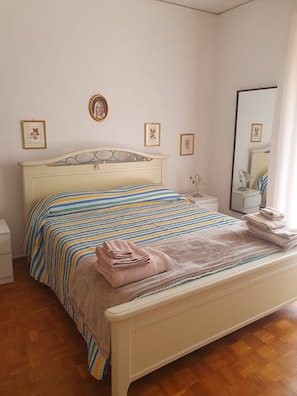 A bedroom with a bed, a bedside table, a mirror, and framed pictures on the wall.