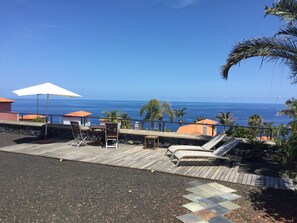 Eine Holzterrasse mit Liegestühlen und einem Tisch, mit Blick auf den Ozean.