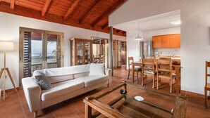 A living room with a sofa, wooden dining table, chairs, and a glass coffee table. - Vacation Home 'Casa Tagoro, Facing The Ocean' with Sea View, Private Terrace and Wi-Fi (Tacoronte)