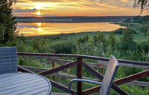 A deck with a view of a sunset over a lake, surrounded by greenery.