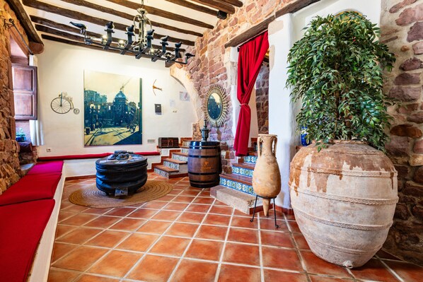 A rustic room with a tiled floor, a large vase, a bicycle wheel decoration, and a painting of a cityscape.