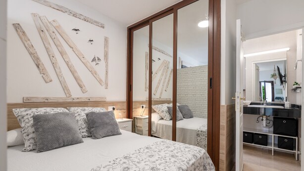 Quarto com duas camas, cabeceira de madeira, espelho, cômoda e parede de tijolos.