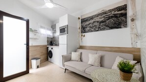 Uma sala de estar moderna com um sofá, uma mesinha redonda com uma planta, um micro-ondas e uma máquina de lavar roupa.