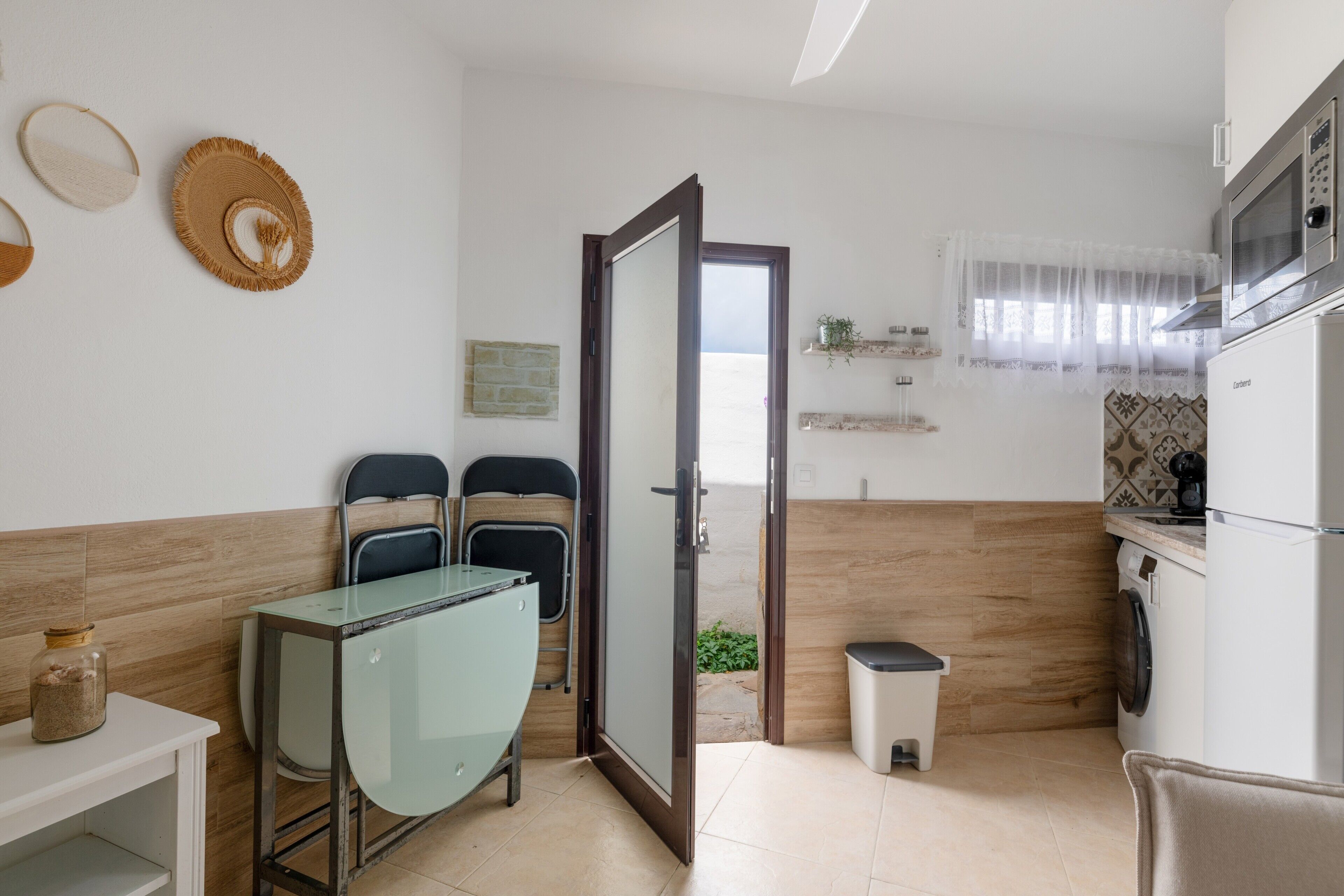 A kitchen with a microwave, a sink, a trash bin, and a door leading outside.