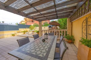 Une terrasse extérieure avec une table et des chaises carrelées, une pergola et des plantes en pot.