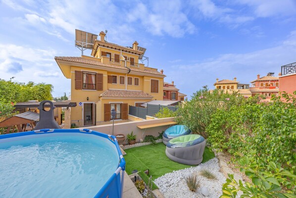 Une propriété résidentielle dotée d’une piscine, d’un jardin avec gazon synthétique et d’une grande maison comportant de nombreux balcons.