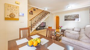 A dining area with a wooden table, a fruit bowl, and a staircase leading to a living room with a sofa. - Holiday Home 'Adosado En Finestrat' with Mountain View, Wi-Fi and Air Conditioning (Finestrat)