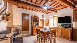A rustic kitchen with wooden beams, a stone fireplace, a dining table with chairs, and a television. - Apartment 'Sotto Gli Archi' with Mountain View (Civitella Paganico)