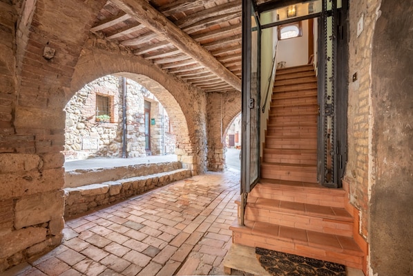 An interior with stone arches, a wooden staircase, and a brick floor.