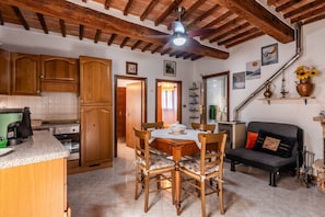 A kitchen with wooden cabinets, a dining table with chairs, a ceiling fan, and a staircase with a shelf holding a vase and a lamp.