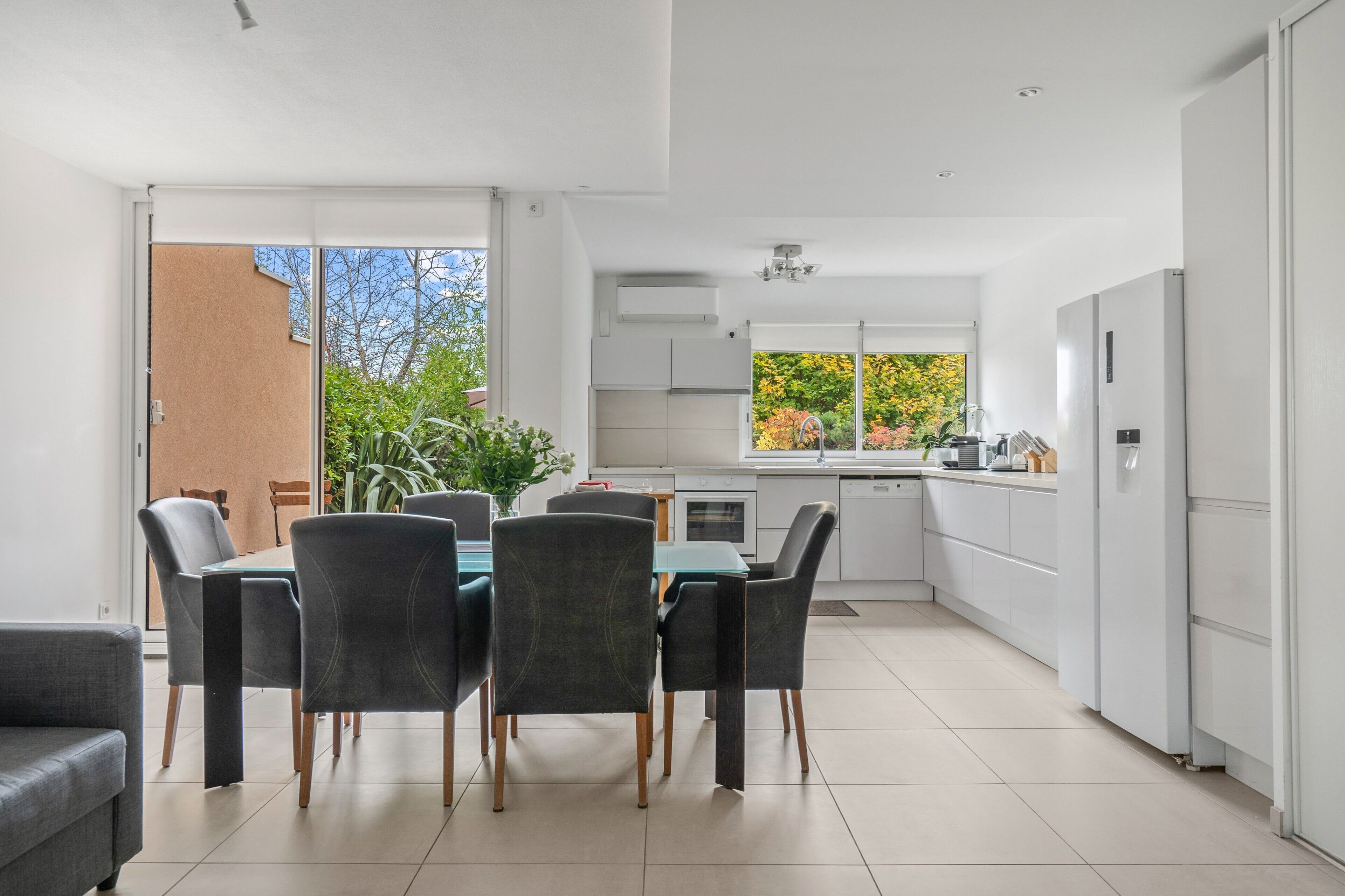 Une cuisine moderne avec des meubles blancs, un coin repas comprenant une table et des chaises, et une porte-fenêtre coulissante donnant sur un espace extérieur.