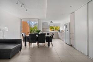 Une cuisine moderne avec des meubles blancs, un coin repas comprenant une table et des chaises, et un canapé gris.