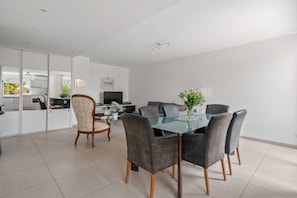 Un salon moderne avec une table à manger en verre, des chaises foncées, un canapé et un téléviseur.