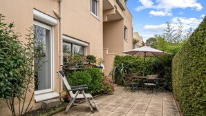 Une terrasse avec une table et des chaises, une plante en pot et une fenêtre.