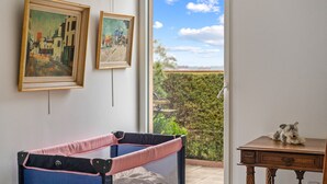 Une pièce avec vue sur un paysage verdoyant, une barrière de sécurité pour bébé et une petite table sur laquelle est posé un ours en peluche.