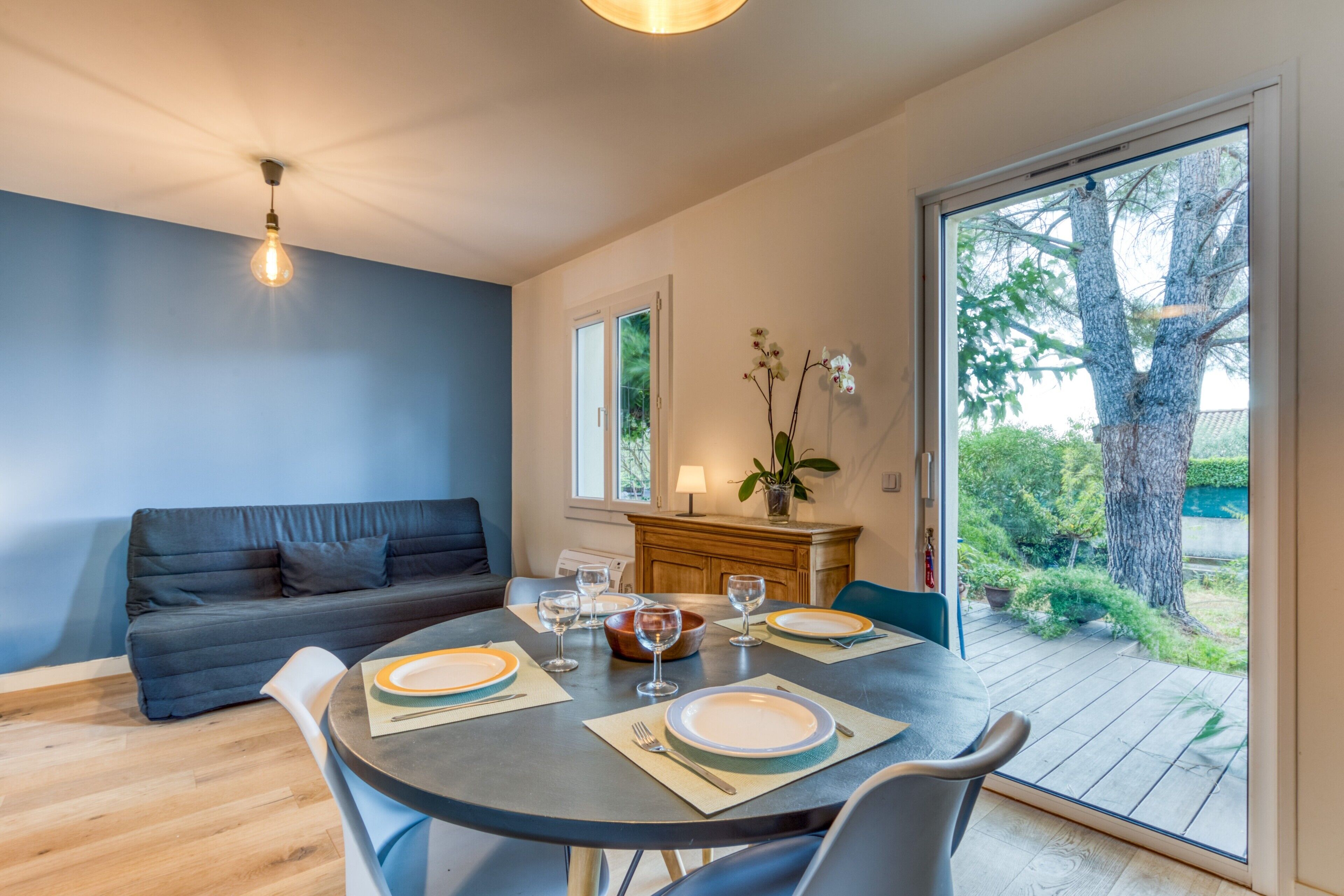A dining area with a round table set for four, a sofa, and a view of the outdoors through a sliding door.