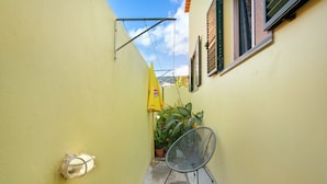 A narrow alleyway with a yellow wall, a potted plant, a metal chair, and a small table with a yellow umbrella. - Holiday Home 'Levada Residence' with Private Terrace, Private Garden and Wi-Fi Access (Funchal)