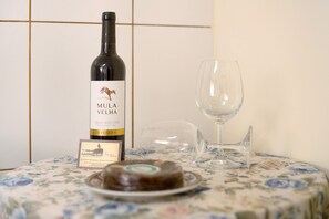 Una botella de vino, una copa y un plato con postre sobre una mesa con mantel de flores.