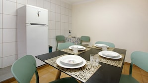 A dining area with a table set for four, chairs, a refrigerator, and a tiled wall. - Holiday Home 'Levada Residence' with Private Terrace, Private Garden and Wi-Fi Access (Funchal)