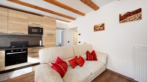 Una cocina moderna con vigas de madera, un sofá color beige con cojines rojos y un radiador blanco.