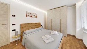 Un dormitorio moderno con cabecera de madera, cama con toallas dobladas, mesita de noche con lámpara y armario.