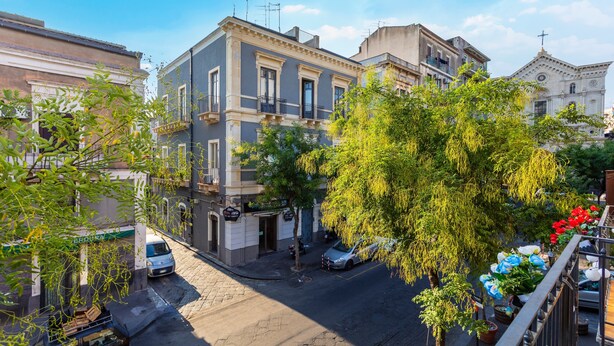 Vista de una calle con edificios, un coche estacionado y un árbol.