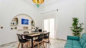 Un comedor con suelo de mármol, una mesa de madera, sillas negras, un sofá verde azulado y una planta en maceta.