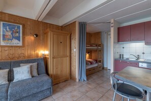 A compact room with a sofa, a bunk bed, a kitchenette, and a wooden wall with a poster.