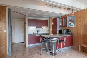 Una cocina compacta con una isla central, taburetes de bar, microondas y cafetera.