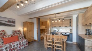 A cozy living room with a sofa, a dining table with chairs, a kitchen area with cabinets and a stove, and a wooden ceiling with exposed beams. - Flaine Studio J2 Apartment with Mountain View and Wi-Fi (Ar âches-la-Frasse)