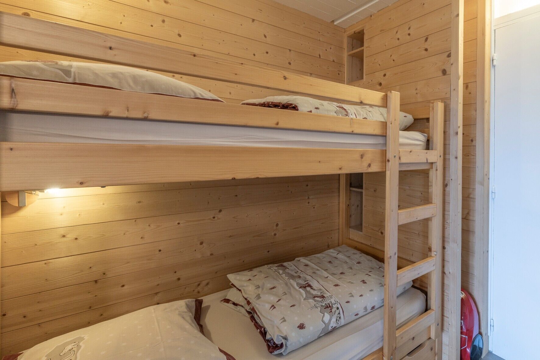 A bunk bed room with wooden walls, a ladder, and a door.