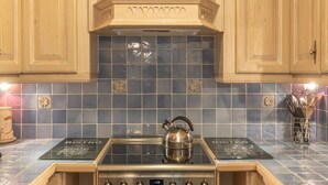 Une cuisine avec des meubles en bois, un dosseret de carreaux bleus et une bouilloire en acier inoxydable posée sur la cuisinière.