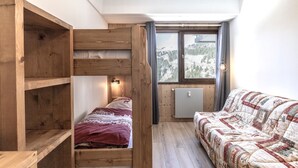 Une chambre avec un lit superposé, un canapé, une fenêtre donnant sur un paysage enneigé et un radiateur.