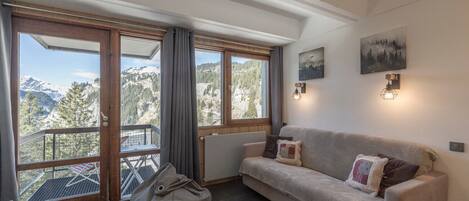 A cozy room with a sofa, a bean bag, and a balcony with a mountain view.