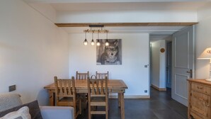 Un coin repas avec une table et des chaises en bois, un luminaire suspendu et un tableau représentant un loup accroché au mur.