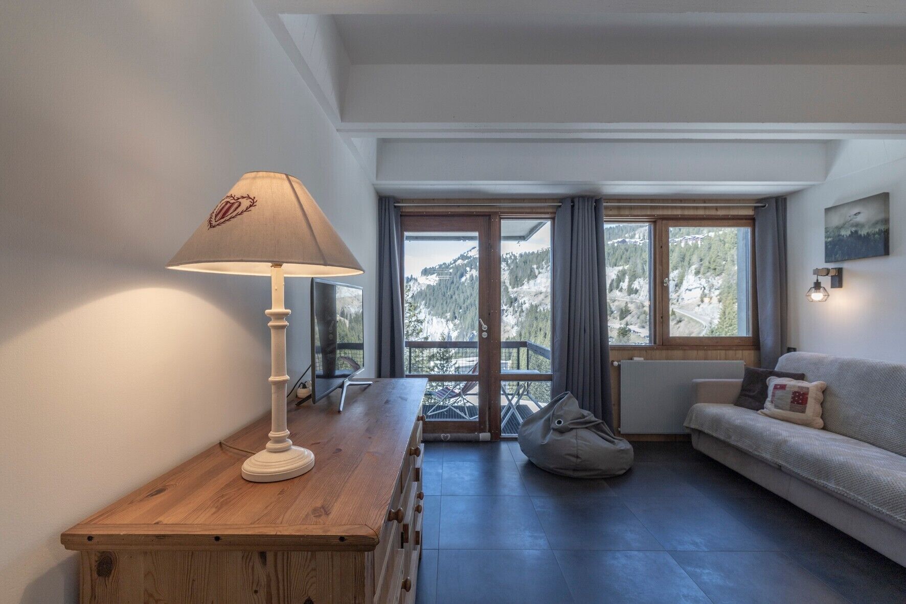 Una sala de estar acogedora con una mesa de madera, una lámpara, un sofá y vistas a una montaña nevada.