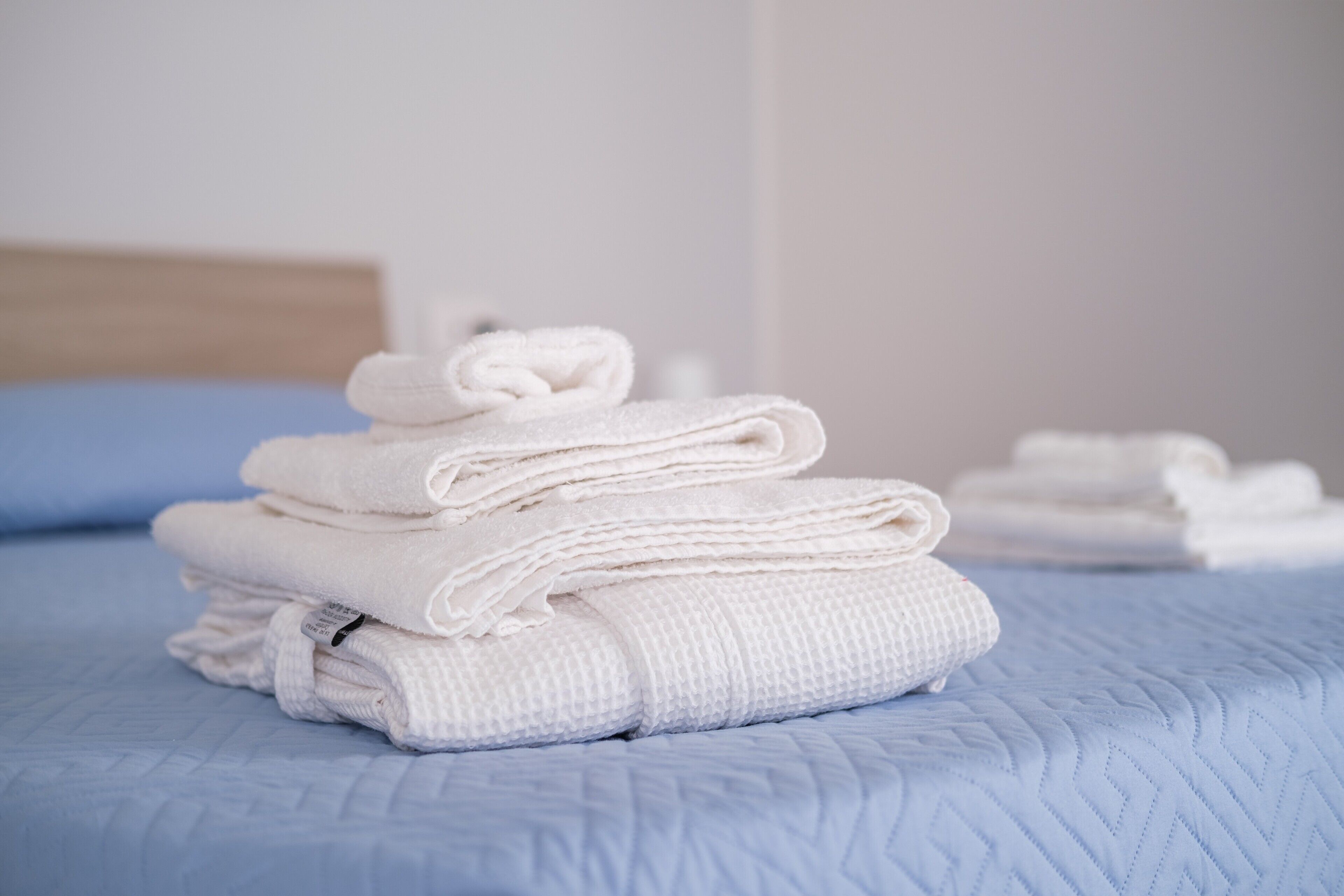Una pila ordenada de toallas blancas sobre una cama con cubrecolcha azul acolchado.