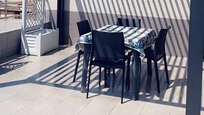 Eine überdachte Terrasse im Freien mit Tisch und Stühlen, einer Pergola und Blick auf ein Gebäude im Hintergrund.