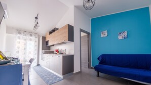 Eine moderne Küche mit Holzausstattung, ein Essbereich mit blauem Tisch und Stühlen sowie ein blaues Sofa in einem Raum mit blauen Wänden.