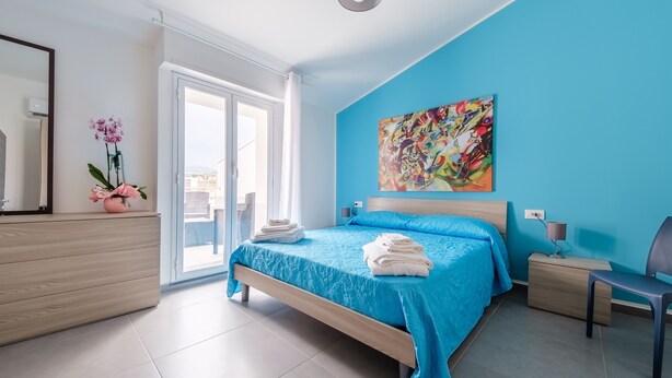 Ein Schlafzimmer mit Bett, Nachttisch, Sessel, einem Gemälde und einer Orchidee im Topf.