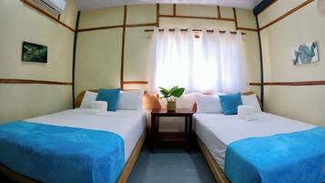 A room with two beds, a small table with a plant, and a window with curtains.