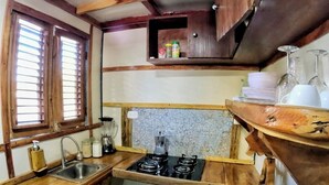 Una cocina compacta con armarios de madera, estufa a gas, lavamanos y ventana con persianas.