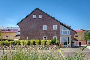 A two-story brick house with a large window on the ground floor, a small balcony, and a stone pathway leading to the entrance. - Strand Loft - Ferienwohnung "strand-loft" in Westerland (Sylt)