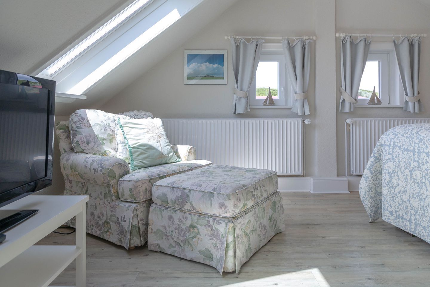 A bedroom with a sloped ceiling, a sofa bed, a TV, and two windows with curtains.