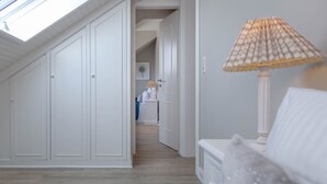 A room with a skylight, a bed with a white headboard, a lamp, and a hallway leading to a bathroom. - Strand Loft - Ferienwohnung "strand-loft" in Westerland (Sylt)