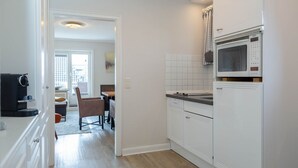 A kitchen with white cabinets, a Bosch microwave, and a dining area with a table and chairs. - Strand Loft - Ferienwohnung "strand-loft" in Westerland (Sylt)