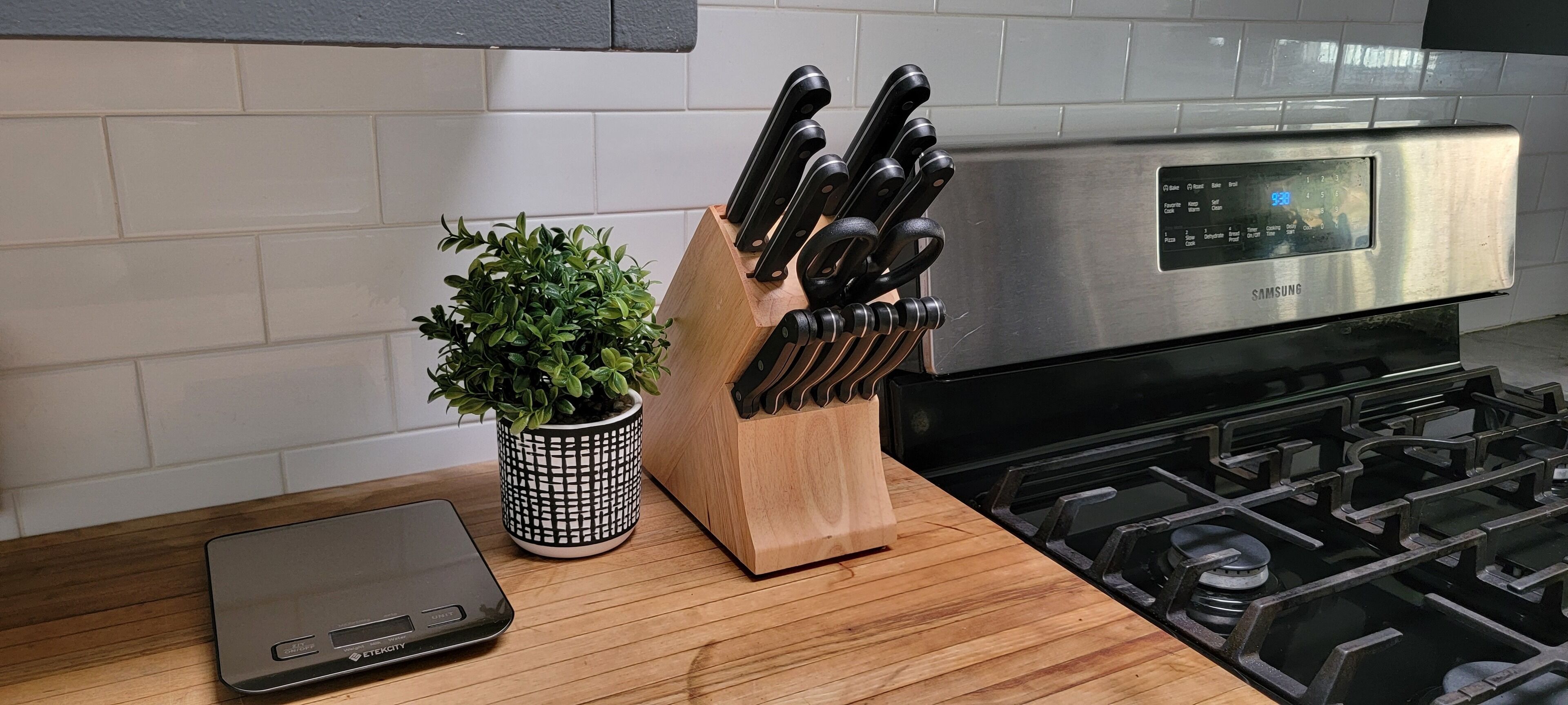 A kitchen counter with a digital scale, a knife block, and a potted plant.