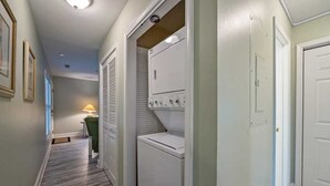 A laundry room with a washer and dryer, a door, and a hallway with a lamp.