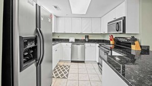 A modern kitchen with white cabinets, a stainless steel refrigerator, a dishwasher, a microwave, and a granite countertop.