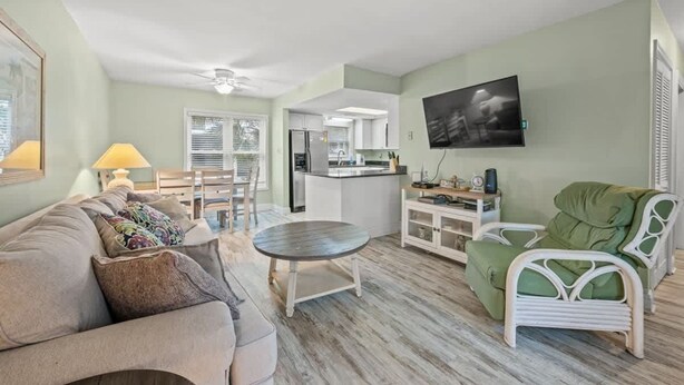 A living room with a sofa, a round table, a green chair, a kitchen area, and a television.